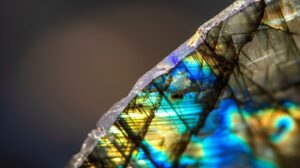 gros plan d'une pierre de labradorite, mettant en valeur sa structure cristalline triclinique avec des reflets métalliques vibrants dans des tons de bleu, vert et or.